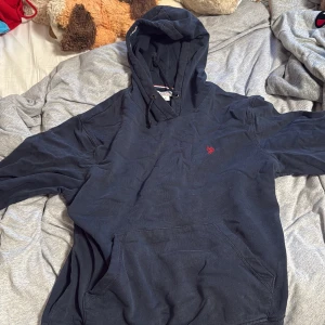 Mörkblå hoodie från U.S. Polo Assn - Säljer en mörkblå hoodie från U.S. Polo Assn i storlek S. Tröjan har huva med snörning, en stor magficka och ett litet rött logobroderi på bröstet. Perfekt för chill dagar och enkel att matcha med jeans eller joggers.