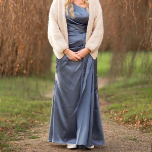 Blå långklänning med slits och oneshoulder - Elegant blå långklänning i satin med oneshoulder och hög slits framtill. Klänningen har omlott-detalj i midjan och ett fint fall. Perfekt för fest eller bal.