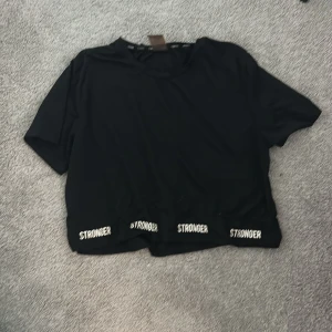 Svart träningströja  - Svart croppad t-shirt från stronger. T-shirten har korta ärmar och en avslappnad passform, perfekt för en sportig look.