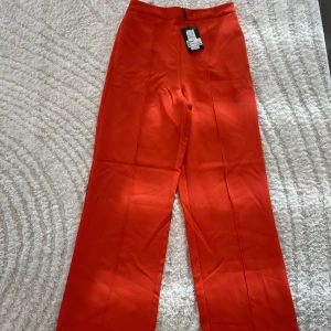 Bossy HW Wide Pant T Tango från Pieces nya prislapp på - Säljer ett par orangea  kostymbyxor från Pieces i modellen Bossy HW Wide Pant T Tango. Byxorna har hög midja och raka, vida ben. Perfekta för dig som vill sticka ut med färg.Kan skicka fler bilder om det behövs 