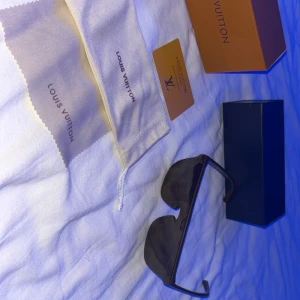 Svarta solglasögon från Louis Vuitton - Säljer ett par svarta solglasögon från Louis Vuitton med breda skalmar och helsvart glas. Klassisk och stilren design, perfekt för dig som vill ha en exklusiv accessoar. Kommer med originalfodral, putsduk och box. Helt nya 