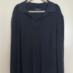 Mörkblå stickad tröja med krage från Riley - Säljer en svart stickad tröja från Riley med klassisk krage och v-ringning. Tröjan har lång ärm och är perfekt för en stilren och enkel look. Passar bra till kallare sommar kvällar. Skick 9/10, knappt blivit använd. Köpt för cirka ett år sedan men inte blivit använd speciellt mycket. Vid minsta fundering skriv till mig. Pris kan alltid diskuteras!