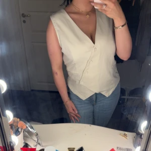 Beige kostymväst med v-ringning - Snygg beige väst med v-ringning och knäppning framtill. Västen har en klassisk kostymskärning och två fickor framtill. Perfekt att styla.