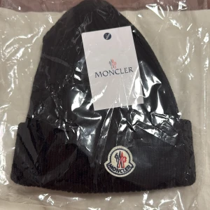 Svart  Moncler mössa - Svart ribbstickad mössa från Moncler med uppvikt kant och Moncler-logga framtill. Klassisk och stilren design som passar perfekt till kyliga dagar. Helt ny, prisen kan diskuteras. 