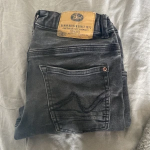 Svarta jeansbyxor från Petrol - Säljer ett par svarta Petrol Travis jeans med klassisk femficksdesign. Byxorna har raka/slima ben och normal passform, med läderpatch bak i midjan. Perfekta för dig som gillar stilrena och bekväma jeans. Storlek: 150 cirka, väl använda men i bra skick, kontakta vid frågor! 