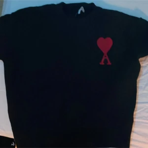 Svart stickad tröja från Ami Paris - Svart stickad tröja från Ami Paris med röd broderad logga i form av ett hjärta och bokstaven A på bröstet. Klassisk rund halsringning och långärmad modell. Perfekt för dig som gillar stilrena plagg med en twist.