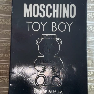 Moschino Toy Boy Eau de Parfum 100 ml - Moschino Toy Boy Eau de Parfum är en unik sommardoft i en unik svart björnformad flaska.                                                Den kostar 900-1000kr beroende på vart man köper men jag säljer den för 500kr. Pris kan diskuteras.                                                                       Flaskan är 100ml och ungefär 95ml är kvar.                                                                       Parfymen hämtas upp.                                         Skriv för mer info!