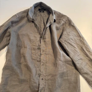 Grön linneskjorta från Massimo Dutti - Säljer en grön skjorta i linne från Massimo dutti. Skjortan har klassisk krage, knäppning framtill och långa ärmar. Perfekt för en avslappnad men stilren look.