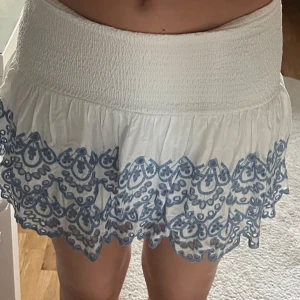 Vit kjol med blå broderi från Lindex - Supersöt vit kjol från Lindex med blå broderade detaljer och volanger. Köpt för 349, men aldrig använd💕 Kjolen har bred smock i midjan och flera lager med broderade kanter. 