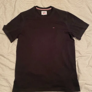 Svart t-shirt från Tommy Hilfiger - Klassisk svart t-shirt från Tommy. T-shirten har rund  Perfekt basic-plagg med stilren design. Inga defekter den är helt ny och orörd. 