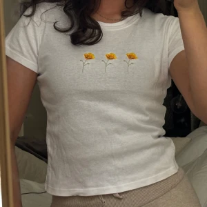 Vit t-shirt med broderade blommor - Vit t-shirt med tre små broderade gula blommor framtill. Knappt använd