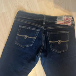 Mörkblå lågmidjade jeansbyxor från pjc rl (Polo Jeans Co Ralph Lauren) - Säljer ett par väldigt lågmidjade mörkblå jeans från pjc rl (polo jeans Co Ralph Lauren) med kontrastsömmar och två bakfickor med dekorativa detaljer. Byxorna har en klassisk femficksdesign och en patch med amerikansk flagga på baksidan. Unika detaljer på knapparna, sömmarna, och på insidan med lapparna. Perfekta att klippa till shorts eller att bära som de är! 🩵     Hittar ingen storlek men skulle säga typ 27 ungefär i midjan och passar mig som är 169 bra i längden. Mäter gärna vid intresse. 