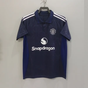 Manchester United bortatröja B. Fernandes 8 - Mörkblå Manchester United bortatröja med vita detaljer och tryck 'B. Fernandes 8' på ryggen. Tröjan har klassisk krage, vita axelränder och klubbmärke på bröstet. Materialet är lätt och andas, perfekt för fotbollsträning eller match.