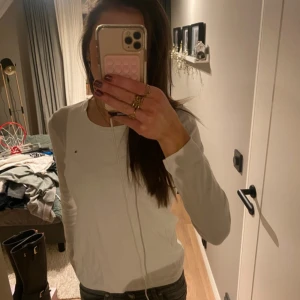 Vit långärmad tröja från Tommy Hilfiger - Säljer en klassisk vit långärmad tröja från Tommy Hilfiger. Tröjan har en rund halsringning och en enkel, stilren design som passar till mycket. Perfekt basplagg i garderoben!