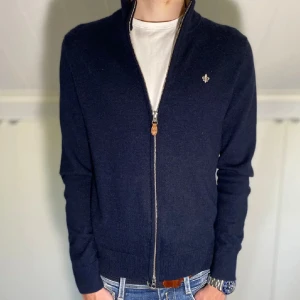 Mörkblå stickad kofta med dragkedja från Morris - Säljer en mörkblå stickad kofta från Morris med hel dragkedja och liten broderad logga på bröstet. Koftan har ribbade muddar och krage med kontrastfärg på insidan. Perfekt för lager-på-lager och stilren look. Nypris: 1799