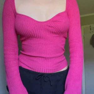 Tröja  - Säljer en tight, ribbad och croppad tröja i stark rosa färg. Tröjan har lång ärm med utsvängda ärmslut och en snygg, fyrkantig urringning. Perfekt för dig som gillar trendiga och färgglada plagg.