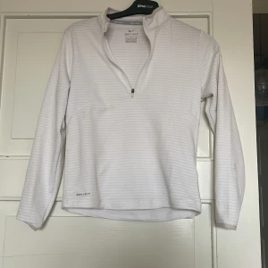 Vit långärmad Dri-Fit tröja från Nike  - Säljer en vit långärmad Dri-Fit tröja från Nike Golf med diskreta horisontella ränder och halv dragkedja framtill. Perfekt för sportiga aktiviteter och tillverkad i funktionsmaterial som andas.
