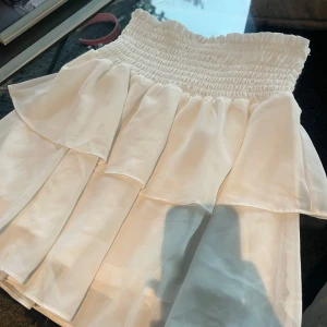 Vit volangkjol  - Supersöt vit kortkjol från Chelsea med flera lager volanger och smock i midjan. Kjolen är luftig och har en flowy känsla, perfekt för varma dagar. Enkel att matcha med olika toppar. Tveka inte att skriva om ni ha ytterligare frågor!😊🫶🩷