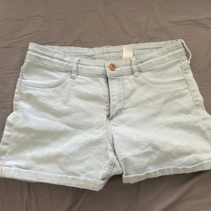 Ljusblå lågmidjade jeansshorts från &Denim - Ljusblå jeansshorts med klassisk femficksdesign och knappgylf. Shortsen har bälteshällor och är tillverkade i ett mjukt denimtyg. Perfekta för varma dagar och enkla att matcha med olika toppar.