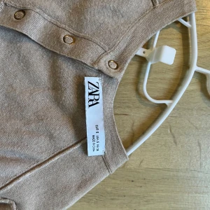 Beige kortärmad topp från ZARA - Säljer en beige kortärmad topp från ZARA med rund halsringning och dekorativa knappar framtill. Mjuk och lättstickad, perfekt för vår och sommar. Enkel att matcha till olika outfits!