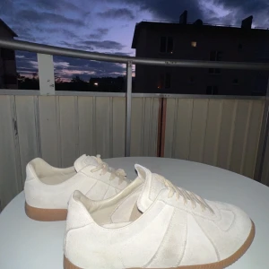 Maison Margiela sneakers med mocka och gummisula - Säljer ett par stilrena Maison Margirla sneakers med ovandel i mocka och klassisk brun gummisula. Skorna har snörning och rund tå, perfekt för en clean och enkel look. Passar till många olika outfits och är riktigt bekväma.