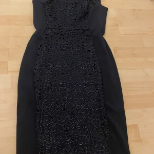 Mörkblå klänning med spetsdetaljer från Enfocus Studio - Säljer en elegant mörkblå klänning från Enfocus Studio med vackra spetsdetaljer och blommigt mönster framtill. Klänningen är perfekt som present till en äldre kvinna eller om man gillar classy dresses 🎀