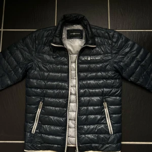 Mörkblå pufferjacka från Sail Racing - Säljer en snygg mörkblå pufferjacka från Sail Racing med snygg design och silvrig insida. Nypris oklart ungefär 2400kr storlek S. 