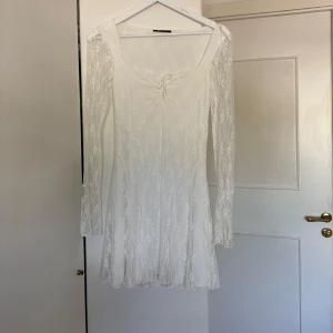 Vit spetsklänning med långa ärmar - Säljer en romantisk vit klänning i spets med långa ärmar och lätt utsvängd kjol. Endast använt en gång. Klänningen har en feminin passform och fina spetsdetaljer över hela plagget. 