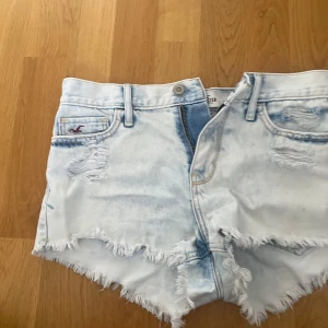 Ljusblå jeansshorts med fransar från Hollister - Säljer ett par ljusblå jeansshorts från Hollister med slitna detaljer och fransig kant. Klassisk femficksmodell med låg midja och råa kanter. Perfekta för sommaren och riktigt snygga till sneakers eller sandaler.