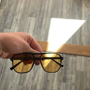 Svarta bågar med gula glas lika Tom Ford  - Snygga solglasögon med svart metallbåge och gula, rektangulära glas. Klassisk pilotstil som ger en cool look och passar perfekt till soliga dagar.