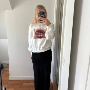 Vit sweatshirt med tryck från Stay - Vit sweatshirt med ett stort tryck av röda läppar och texten 'STAY' på framsidan. Tröjan har rund halsringning och långa ärmar med ribbade muddar. Perfekt statement-plagg för dig som vill sticka ut.