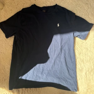 Mörkblå t-shirt från Polo Ralph Lauren - Säljer en klassisk mörkblå t-shirt från Polo Ralph Lauren med vit broderad logga på bröstet. T-shirten har rund halsringning och är tillverkad i mjuk bomull. Perfekt för en stilren och avslappnad look.