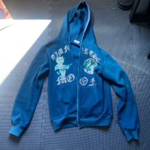 Mörk blå hoodie från Aim for the moon - Säljer en blå hoodie från Aim For The Moon i storlek M. Tröjan har dragkedja, huva och två fickor framtill. Framsidan är dekorerad med rhinestone och tryck av en jordglob och en figur. Tröjan är i mycket bra skick och har inte använts mycket då den inte passar mig längre.