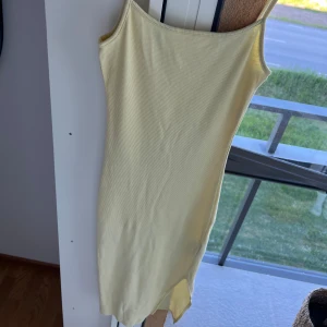 Ribbad långklänning - Säljer en ljusgul ribbad långklänning med smala axelband och rak halsringning. Klänningen har en tight passform och är perfekt för varma dagar. Enkel och stilren design som är lätt att matcha.