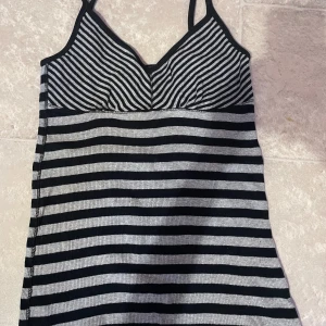 Svart och grå randig klänning med smala axelband - Säljer en stickad linne med smala axelband i svart och grått. Linnet har ett randigt mönster och en figurnära passform upptill. Perfekt för en avslappnad stil.