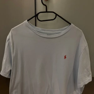 Ljusblå t-shirt från Polo Ralph Lauren - Säljer en ljusblå t-shirt från Polo Ralph Lauren med klassisk röd broderad logga på bröstet. T-shirten har rund halsringning och är kortärmad. Perfekt för en stilren och avslappnad look.