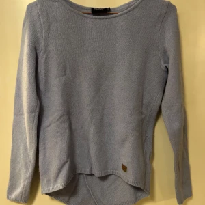 Ljusblå stickad tröja- Holebrook - Mysig ljusblå stickad tröja från Holebrook med rund halsringning och längre bakstycke. Tröjan har långa ärmar och en liten logodetalj nertill.