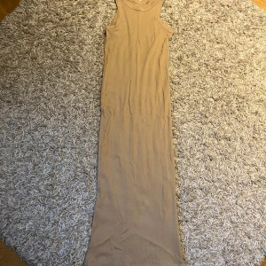 Beige ribbad långklänning - Säljer en beige ribbad långklänning i ärmlös modell. Klänningen har en tight passform och rund halsringning, perfekt för en stilren och enkel look. Passar dig som gillar minimalistisk stil.