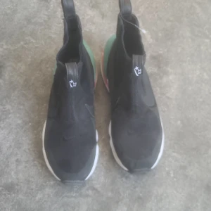 Svarta Nike Zoom Air sneakers - Snygga svarta Nike sneakers med Zoom Air-teknologi. Skorna har en unik design med färgglada detaljer i grönt och rött på sulan. Perfekta för en sportig look. Lite slitage men har sett andra i samma klass gå för 5000 för samlare svår modell att hitta! 