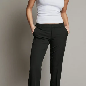 Svarta kostymbyxor med normal passform - Snygga svarta kostymbyxor med klassisk rak passform och diskreta fickor framtill. Byxorna har hällor för bälte och stängs med dragkedja och knapp. Perfekta till en stilren look.