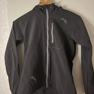  Lundhags jacka - Säljer en mörkgrå ackafrån Lundhags med dragkedja och huva. Jackan har en praktisk bröstficka med dragkedja och är tillverkad i en blandning av polyamid och lycra för extra komfort och flexibilitet.  Stretchig och skön, gråsvart stl 36