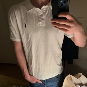Vit pikétröja från Polo Ralph Lauren polo - Klassisk vit pikétröja från Polo Ralph Lauren med blå broderad logga på bröstet. Tröjan har krage, knappar vid halsen och korta ärmar. Perfekt för en stilren och sportig look.