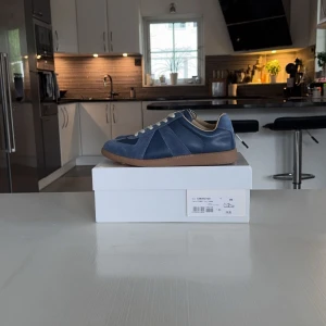 Maison margiela gats - Säljer ett par stilrena blå sneakers från Maison Margiela med vita snören och beige/brun sula. Skorna har en mix av mocka och skinn, klassisk design och rund tå. Skick 10/10. Pris kan diskuteras vid snabb affär. Storleken är 43 men passar även om du har 44.