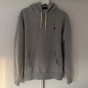 Grå hoodie från Polo Ralph Lauren - Säljer en klassisk grå hoodie från Polo Ralph Lauren  och broderad logga på bröstet. Tröjan har känguruficka och mjukt material, perfekt för en avslappnad stil. Använd 3 ggr och kommer inte till användning nypriset ligger på 2200kr