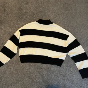 Svartvit randig croppad stickad tröja - Säljer en croppad stickad tröja med breda svarta och vita ränder. Tröjan har lång ärm och hög hals. Perfekt för dig som gillar en trendig och avslappnad stil. Den har en liten fläck på sig(tredje bilden) och lite trådar som sticker ut men inget man märker när man har på den (tycker jag)