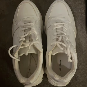 Vita sneakers från Attitude - Snygga vita sneakers från Attitude med klassisk snörning. Perfekta för en stilren look. Skorna har en rund tå och är tillverkade i syntetmaterial. Använda en gång. Små i storleken.