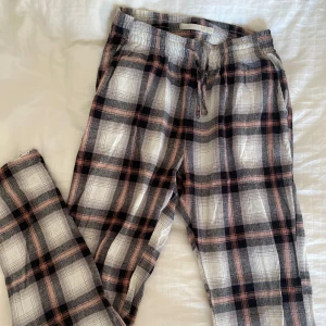 Rutiga pyjamasbyxor  - Säljer ett par rutiga pyjamas i svart, vitt och rosa med dragsko i midjan. Byxorna är uppsprättade längst ner pga att de va för korta (se bild), annars bra skick 