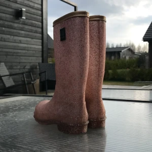 Glittriga rosa gummistövlar från Petit - Säljer ett par höga rosa gummistövlar från Petit med massor av glitter. Perfekta för regniga dagar och har en klassisk stövelmodell med rund tå. Stövlarna är riktigt snygga och sticker ut med sitt glittriga utseende.
