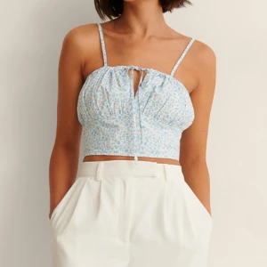 Blommig blå och vit linnetopp - Söt blommig linnetopp i blått och vitt med smala axelband och knytning framtill i strl 36