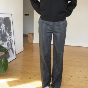 Grå randiga kostymbyxor - Snygga grå kostymbyxor med diskreta vita ränder. Byxorna har en klassisk straight passform och är perfekta för en stilren look. Mid weist.